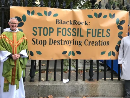 Two faith leaders standing in front of banner reading 'Stop Fossil Fuels'