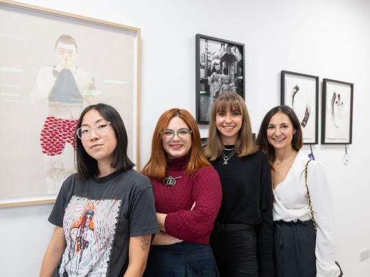 Group of four women with framed prints in the background.