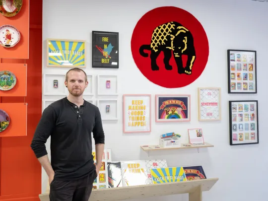 Man with framed prints on a wall in the background