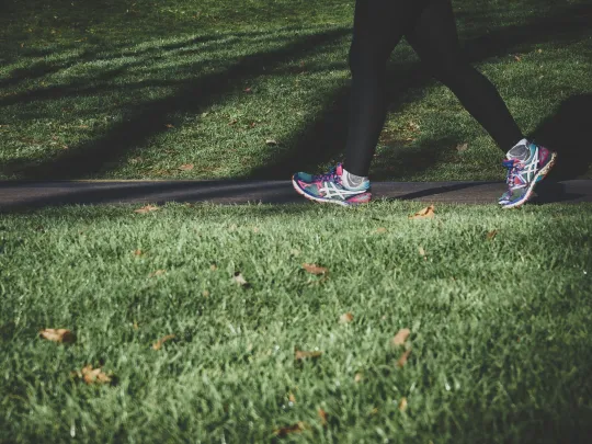 Legs of a person walking alone on an empty grass path