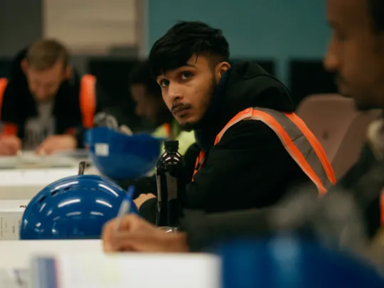 A young man looks up while concentrating in a classroom filled with other students.