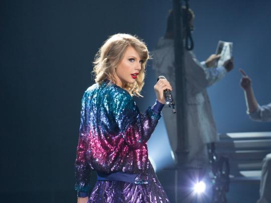 Taylor Swift holding a mic and wearing a shinny jacket
