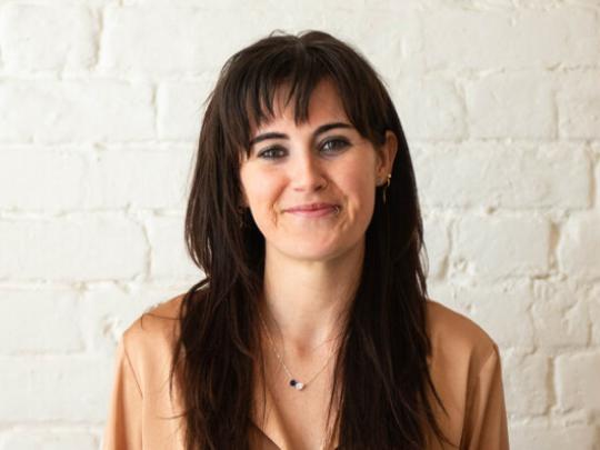 Person with long hair smiling and looking at the camera.