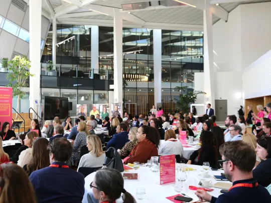 Large group of people sitting at tables in City Hall's London Living Room looking at the stage