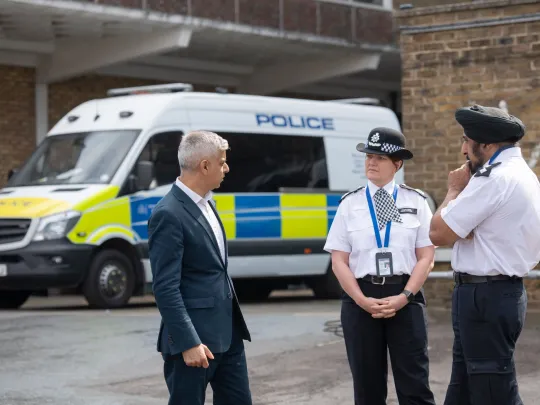 Sadiq Khan speaking to two police officers, stood in front of a police van
