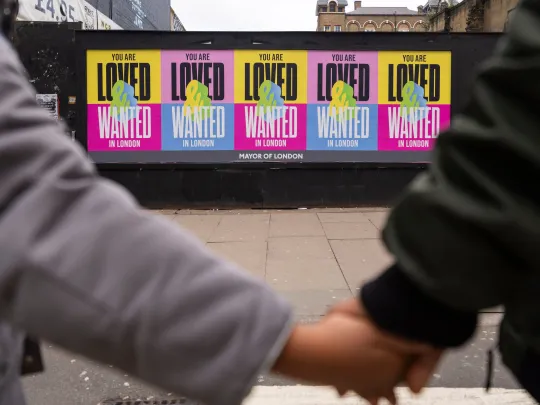 Two people holding hands in front of Loved and Wanted posters