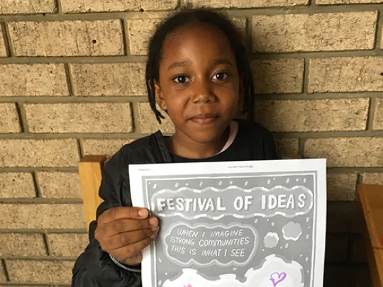 Young girl poses for photo with a Festival of Ideas poster she made