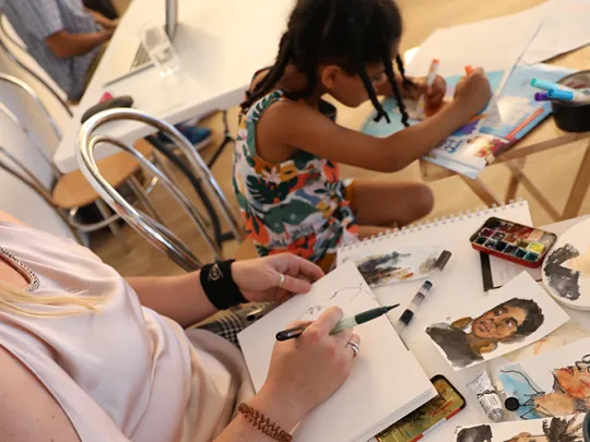 Woman painting, surrounded by pictures, pens and paper. 