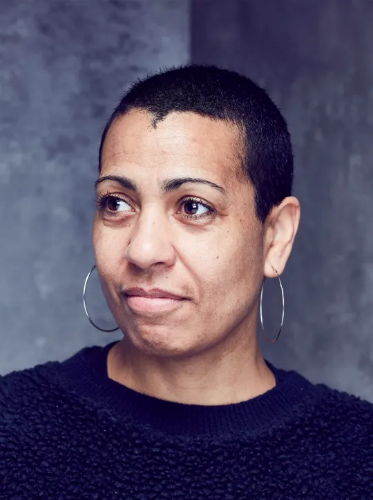 A headshot of the artist Helen Cammock, who is mixed race and has short dark hair. She is wearing silver hooped earrings