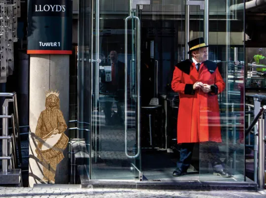 A photograph of a drawing of a child, with a crown and an African mask wearing a crown with a drum on a strap slung around their neck and is holding drum sticks, overlayed on the front of a modern building with glass doors with a doorman wearing a red, cloak jacket and black top hat.