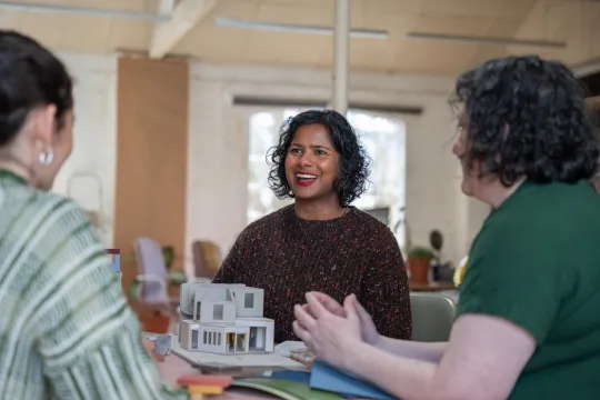 Person smiling at two other people with an architectural model in their hands
