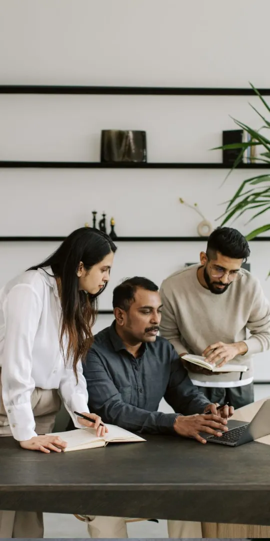 Two colleagues taking notes whilst a third colleagues explains information on a screen