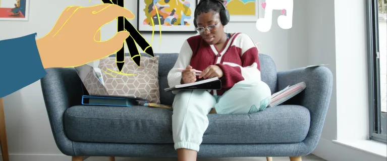 A young person sitting on a blue couch wearing headphones, whilst writing in their notepad.