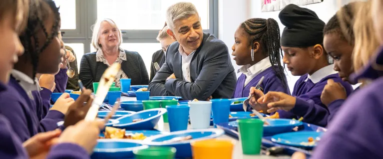 Sadiq Khan sits at a lunch table and talks with pupils in a primary school 