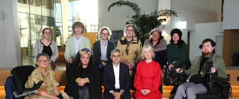 Group of 11 people, with two people in wheelchairs sat on benches looking at the camera.