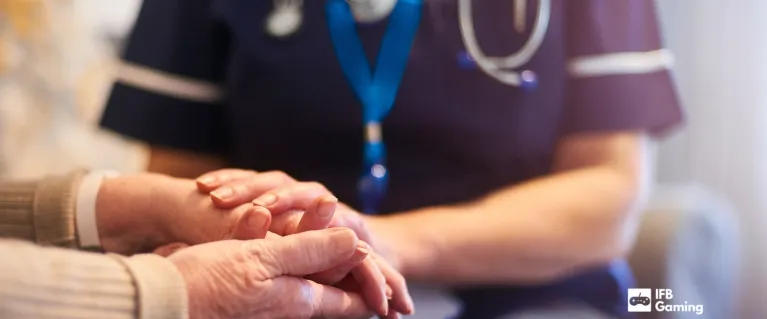 A nurse holding an older persons hands with the IFB Gaming logo in the corner