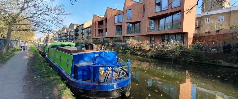 Moored blue and green canal boat with mixed architecture to the opposite side of the canal.