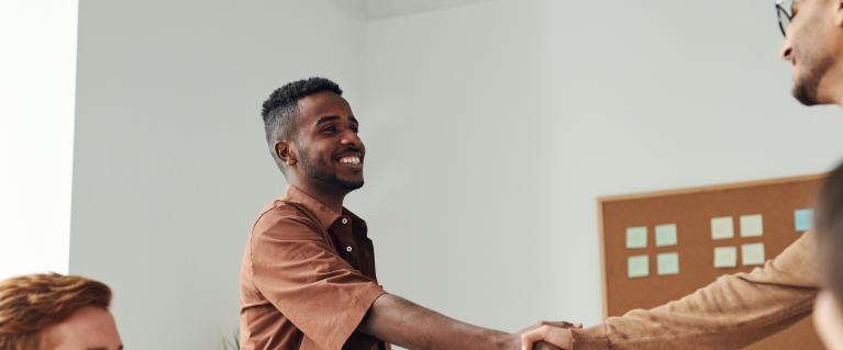 Man in a brown shirt shaking hands with another person upon meeting.