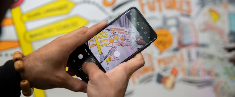 Young person taking picture of Stronger Future board with mobile phone