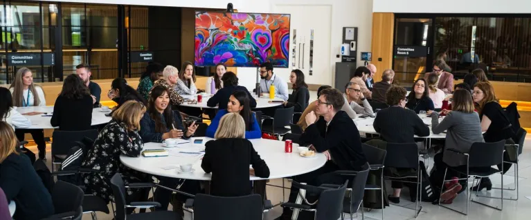 Small groups of people talking while sitting at round tables in a conference room