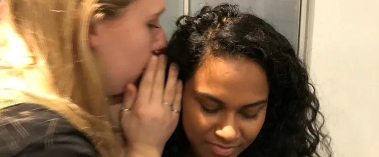 A young woman whispers in anothers ear