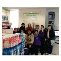 a group of older people strike a pose in a pharmacy, they wear scarves and coats, wave and smile to camera.