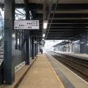 Shot taken from the bottom of the stairs at a train station platform, looking down a rail line. There are two people visible towards the end of the platform