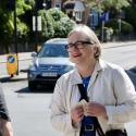 Caroline Russell campaigning for more push buttons on street crossings across London. She is smiling, wearing a white jacket and looking off to the left of the camera engaging with a Londoner. A car is visible in the background. 