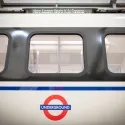 An image of a London tube railcar taken from the outside of the carriage. There are three windows visible, as well as the iconic TfL logo. 