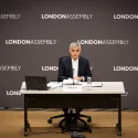 Sadiq Khan sitting at a table in front of a background with London Assembly on it