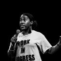 Monochrome image of a live performer on stage holding a microphone