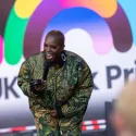 Host on stage with microphone, smiling against UK Black pride rainbow backdrop