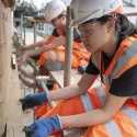 Young construction trainees in orange construction clothes building a wall