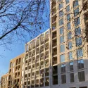 Mid-rise building of flats with blue sky in background and trees in foreground