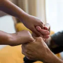 A carer supports an older person, holding their hands.