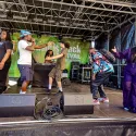 Several performers and a DJ are on an outdoor stage performing at the Music is Black Festival