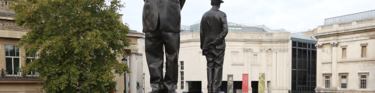 A bronze statue of two men wearing hats on the fourth plinth of Trafalgar Square by Samson Kambalu
