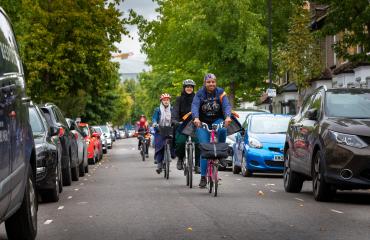 A group of women cycling along rows of parked cars.