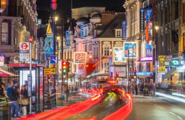 An image showing a lively London street at night with people out and about.