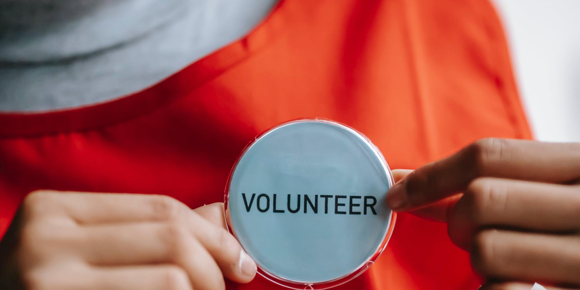 Person in warm orange t-shirt holding a volunteer badge