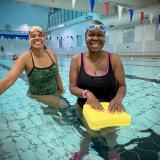 Two ladies in the water, smiling, one holding a float